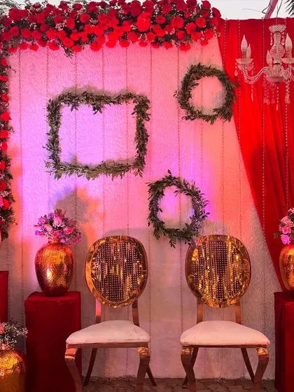 A quirky and fun photo booth with a red and white theme. The design includes framed greenery, chandeliers, and elegant gold chairs, offering a stylish spot for pictures.