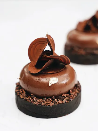 A beautiful chocolate tart with delicate shavings on top. The clean, white background puts all the focus on the dessert's intricate details and rich, glossy finish.