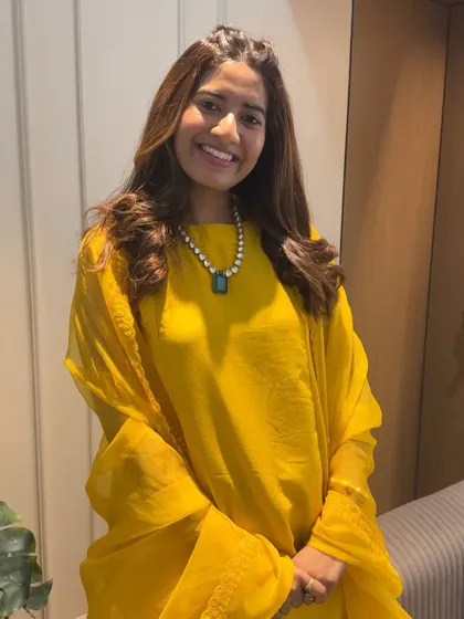A happy client ready for the Haldi party. Her hair is styled beautifully, and the look complements her pearl and emerald necklace.