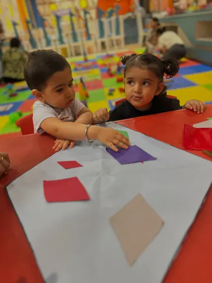 Two children collaborate on a craft project, learning to share space and materials.
