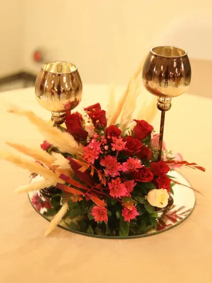 A romantic centerpiece for a cocktail event, featuring red roses, pampas grass, and elegant candle holders on a mirrored base.