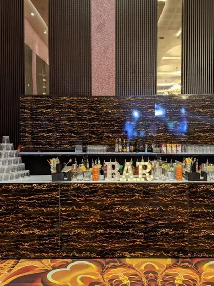 This sleek, marbled-finish bar counter offers a modern and luxurious feel for indoor events. It's fully stocked and ready to serve, complete with a lit 'BAR' sign and glassware towers.