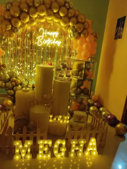 An elegant birthday setup with a gold and peach balloon arch over a gold shimmer curtain.