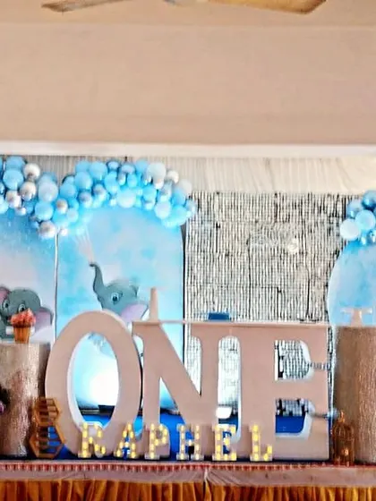 A sweet baby elephant theme for Raphael's first birthday. This setup features a sky-blue backdrop, multiple elephant cutouts, and a silver and blue balloon garland.