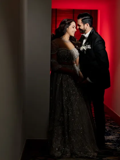 A moody and romantic portrait in a hallway. The dramatic red light in the background creates a passionate atmosphere, while the soft light on the couple highlights their intimate connection. This is a great example of using creative lighting indoors.