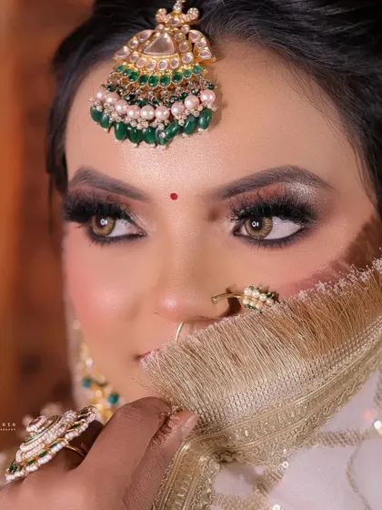 A mysterious and alluring close-up, with the bride peeking over her golden dupatta. The focus is entirely on her expressive eyes and maang tikka.