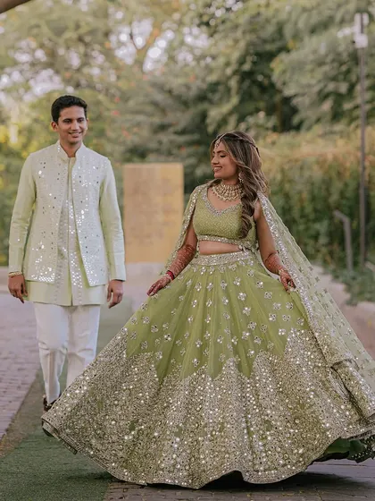 The bride twirls in her stunning green lehenga, her groom looking on with a smile. This shot captures the movement and beauty of her outfit.