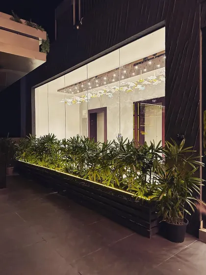 The exterior view of an indoor section of the rooftop restaurant, seen from the terrace. A long planter filled with lush greenery separates the spaces while maintaining a visual connection.