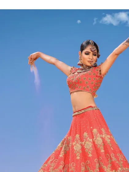 A dramatic shot of the coral-red zardosi lehenga, capturing the bride's powerful and celebratory spirit against a brilliant blue sky.