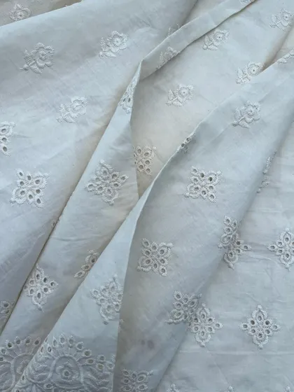 This white cutwork cotton fabric with a geometric buti design is perfect for creating elegant and breathable outfits for any occasion.
