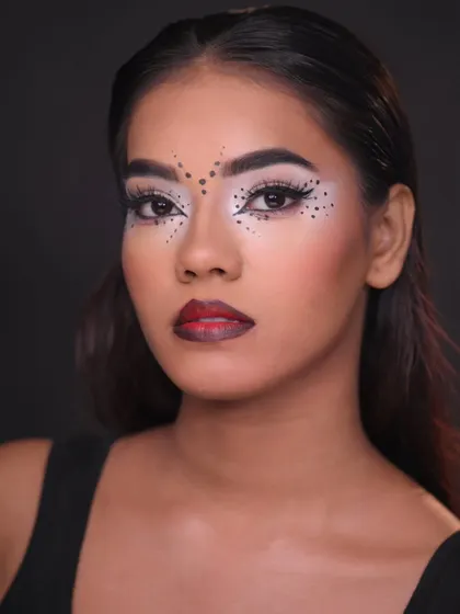 A graphic, tribal-inspired makeup look with bold black dots and white accents, showcasing precision and creativity.