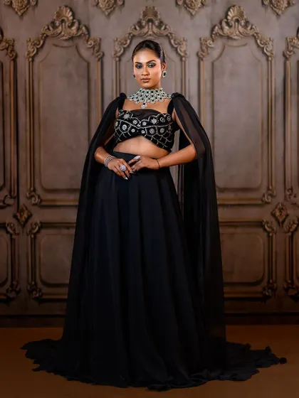 A powerful stance in a modern black lehenga. The dramatic cape sleeves and statement jewellery make this a truly memorable reception look.