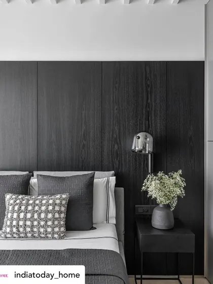 A close-up of a bedroom detail from a project featured in India Today Home. The dark wood paneling and textured grey bedding create a sophisticated, masculine feel, while the chrome bedside lamp adds a modern touch.