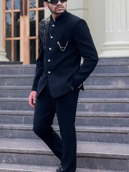 A black Jodhpuri suit with a unique gold and silver embroidered design resembling a peacock feather, complete with a stylish pocket chain.