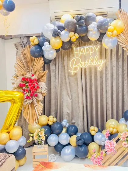 A stylish 17th birthday party decoration with a modern-boho theme. The setup includes a circular frame with a balloon garland, a 'Happy Birthday' neon sign, and large '17' foil balloons, accented with dried palm leaves.