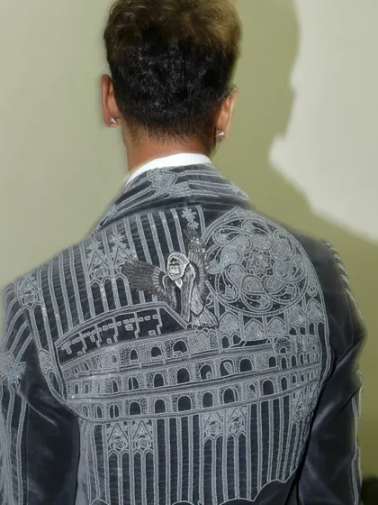 The back of Sarang's grey velvet tuxedo, revealing a striking embroidered narrative of celestial figures and architectural elements. This is wearable art with a deep philosophical undertone.