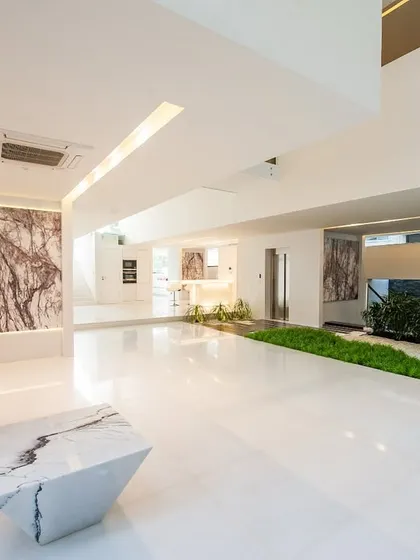 The guest level at Neeti's residence is a bright, expansive space defined by white marble floors and feature walls. A narrow strip of green landscaping cuts through the floor, bringing an organic element into the minimalist interior.