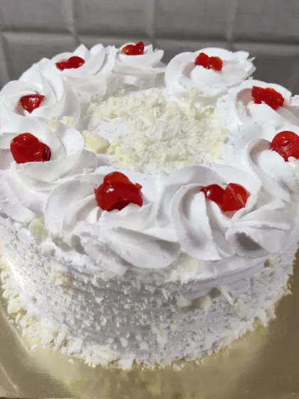 A classic white forest cake. It's decorated with whipped cream rosettes, white chocolate shavings, and cherries.