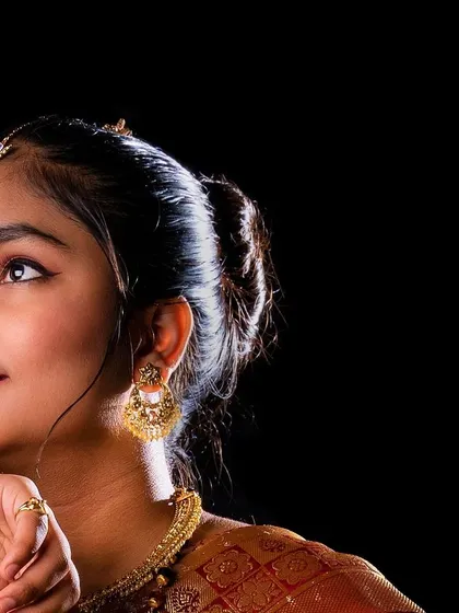 A classic profile shot that elegantly displays the traditional hairstyle and gold earrings. The dark background and focused lighting create a timeless and graceful portrait.