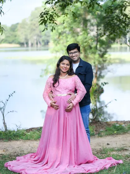 A happy couple posing by a lake in a lovely pink gown.