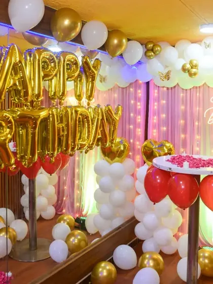 A festive birthday decoration setup with gold "Happy Birthday" balloons and red and white balloon columns.