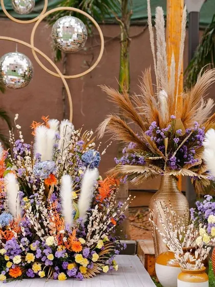 A close-up of the colorful floral arrangements for a boho-themed Mehendi. The mix of different flowers and dried grasses, along with disco balls, creates a fun and eclectic look.
