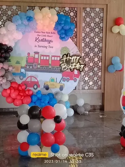 A train and car themed 2nd birthday party. This decoration features a custom backdrop with a train, a balloon arch, and a car-themed cutout.
