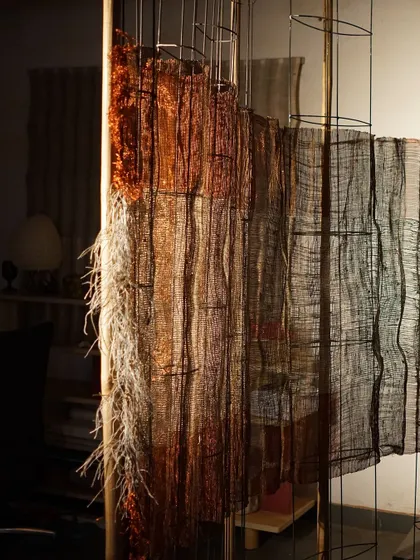 A detail of a woven sculpture from 'Cu+Fibers', showing the transition between different fibers and weaving techniques. The frayed edges and loose threads are an intentional part of the design.