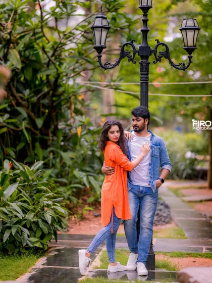 A romantic pose by a vintage-style lamppost. The couple's coordinated casual outfits look stylish against the lush garden backdrop.