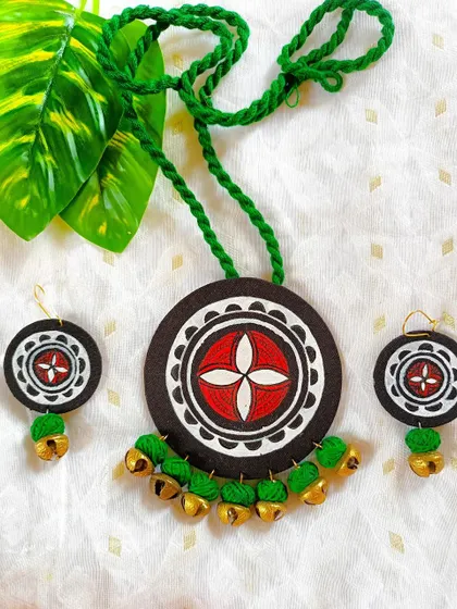 This hand-painted fabric necklace features a traditional Bengali 'alpona' design with ghungroo bells. The green thread adds a festive touch, making it ideal for cultural events.