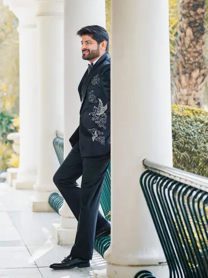 A stylish portrait of the groom leaning against a pillar. This candid-style shot captures his relaxed yet sophisticated look for the reception.