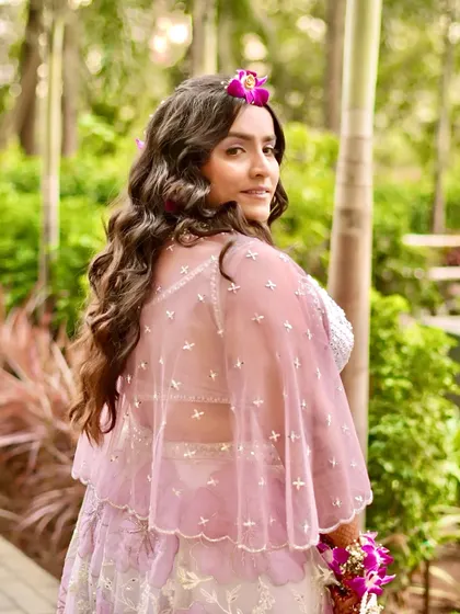 A back profile showing her beautiful wavy hair and the sheer cape of her outfit. The entire look is fresh, modern, and festive.