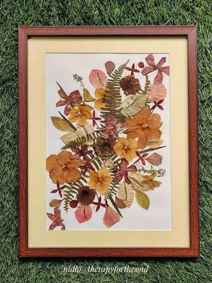 A larger pressed flower arrangement in a wooden frame, displayed against a vibrant green background.