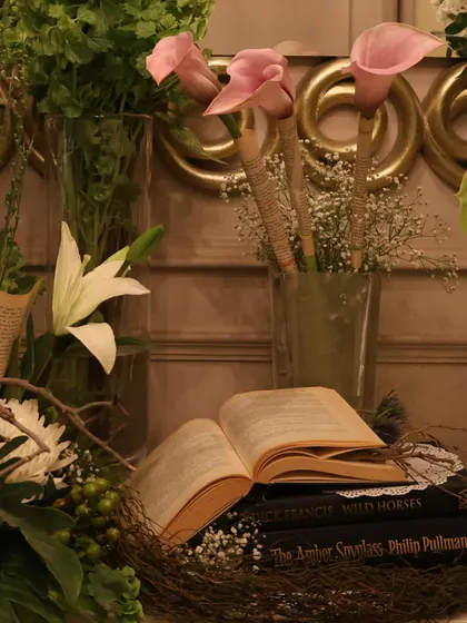 Pink calla lilies and white lilies rise from vases, set against a backdrop of antique books and delicate baby's breath. This arrangement combines modern elegance with vintage charm.