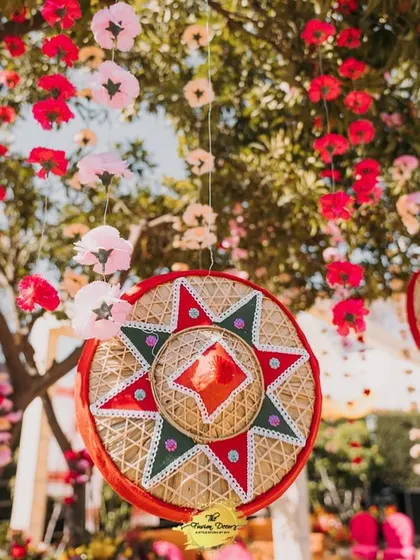 A close-up of a decorative hanging element from the Assamese Haldi. A traditional Jaapi is beautifully embellished and surrounded by hanging paper flowers, celebrating the region's rich craft heritage.