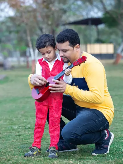 A father teaches his young son how to play a toy guitar. This hands-on, interactive moment makes for a wonderful and memorable photograph.