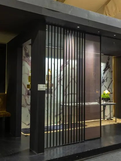 Another view of the 'walk-along' gallery for JB Glass. The design uses layers, lighting, and contrasting materials to create visual depth and draw attention to the intricate details of the glass door and partition systems on display.