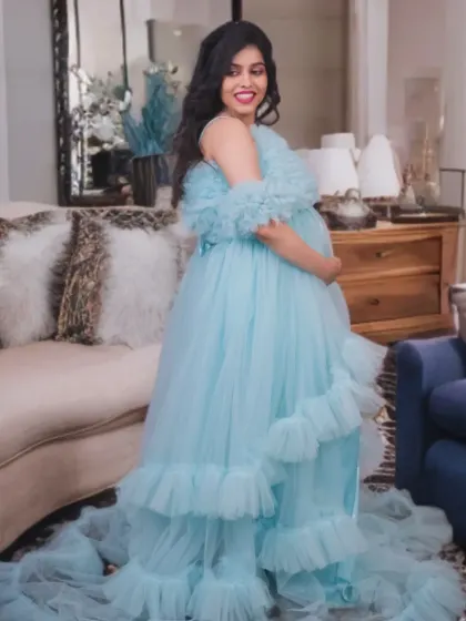This light blue off-the-shoulder gown features soft ruffles and a long train. It's a perfect choice for an airy and feminine look, shown here in a comfortable indoor setting.