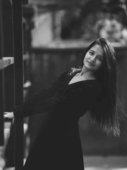 A simple and elegant black and white portrait of a woman with long hair, leaning against a wooden structure. Her direct gaze and the clean composition make for a classic and engaging headshot.