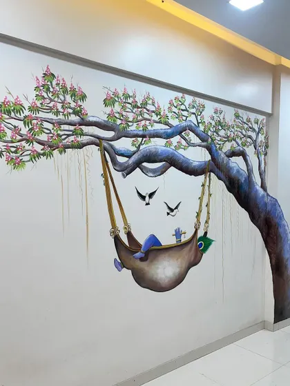 This realistic wall mural of Baby Krishna sleeping in a swing under a tree brings a sense of calm and innocence to the room.
