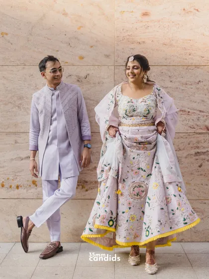 A full-length shot of the couple in their beautiful, coordinated pastel outfits for their Haldi ceremony, showing off the intricate floral embroidery.