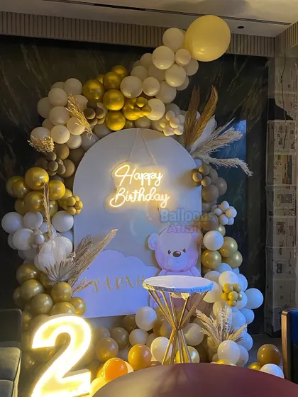 A cozy teddy bear theme for a second birthday. This setup uses a neutral color palette of white, gold, and brown balloons, with a cute bear graphic and a light-up number '2'.