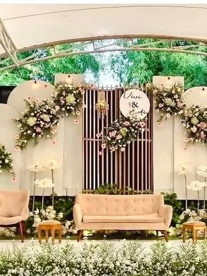 This engagement stage setup is perfect for an outdoor venue. It features modern white arched panels, comfortable lounge seating, and beautiful floral arrangements that complement the natural surroundings.