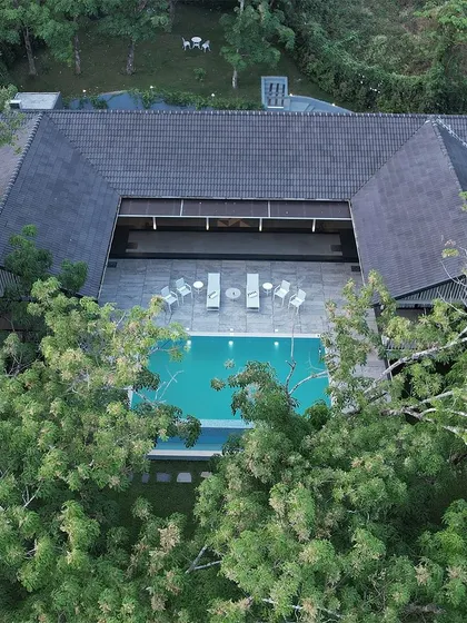An aerial view of the pool and deck at 'The Leaf' in Poomala. The U-shaped building cradles the common area, offering privacy while maintaining a strong connection to the surrounding forest.