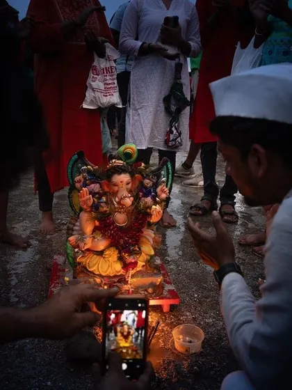 A devotee takes a photo of a small Ganesha idol before its immersion, a modern act of reverence within an ancient tradition.