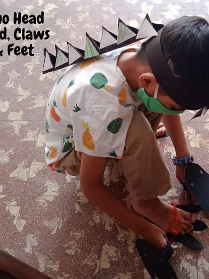 A child transforms into a dinosaur with a handmade headband, claws, and feet. Dress-up and pretend play are powerful tools for learning, allowing children to embody the concepts they are exploring and deepen their understanding.