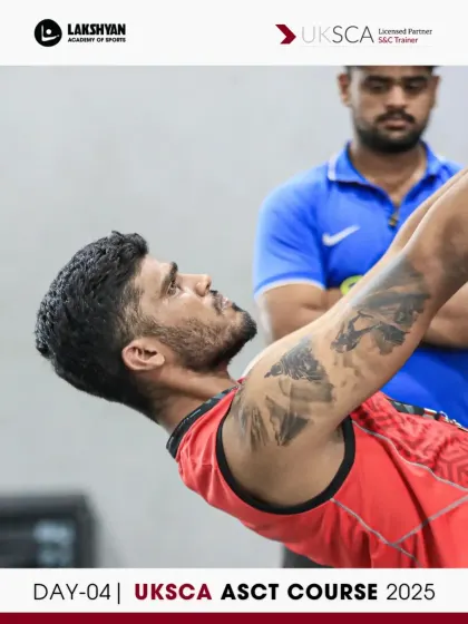 A coach observes and provides feedback as a participant performs a bodyweight exercise, focusing on control and stability.