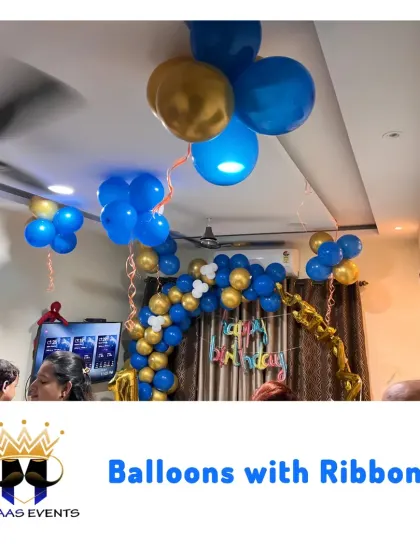Balloons with ribbons hanging from the ceiling create a fun and celebratory atmosphere. This setup in blue and gold is perfect for a boy's birthday party at home.