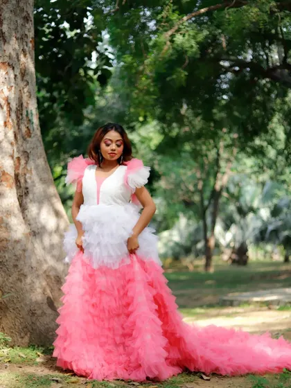 A full-length standing pose in the pink gown, shot outdoors. The makeup is designed to look beautiful and polished in natural daylight, ensuring the model stands out against the green background.