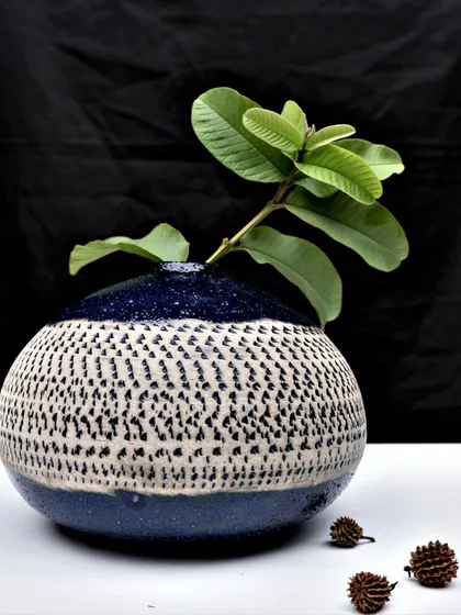 A finished, textured pot serving as a simple vase. The contrast between the deep blue glaze and the dotted white pattern creates a beautiful home for a single green branch.